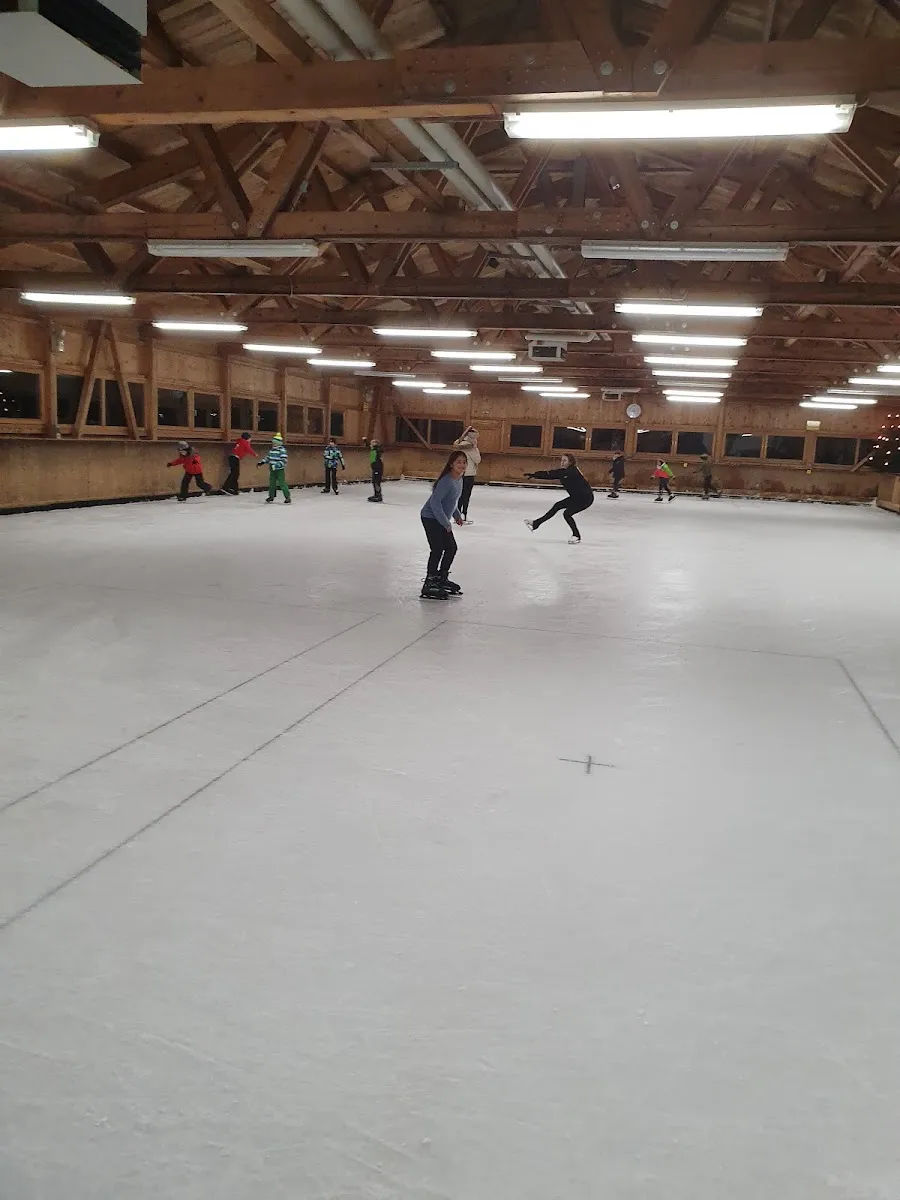 A public skating session in the timber-roofed hall: skaters spread out across the ice under wooden roof trusses. — Eishalle Freyung