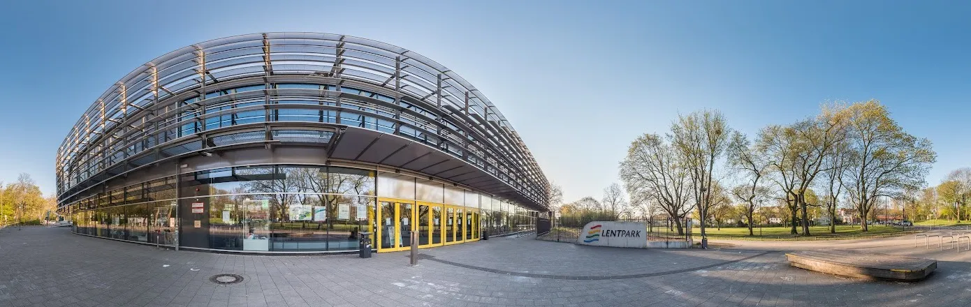 Die geschwungene Glas-und-Stahl-Front des Lentparks mit den gelben Eingangstüren und dem Lentpark-Schild neben dem Park (Ausschnitt aus dem 360-Grad-Foto des Eintrags). – Eishalle Lentpark