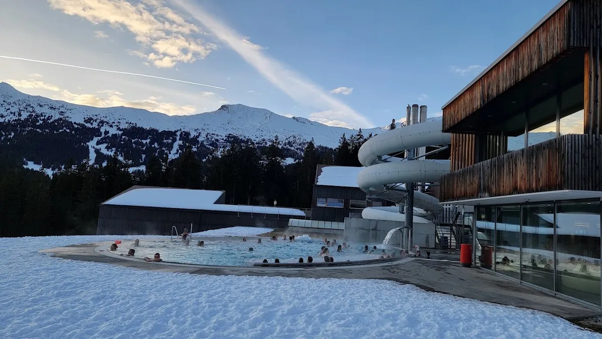 The Sportzentrum Lenzerheide building in winter, with the outdoor thermal pool and the water slide in front of it — Eishalle Sportzentrum Lenzerheide