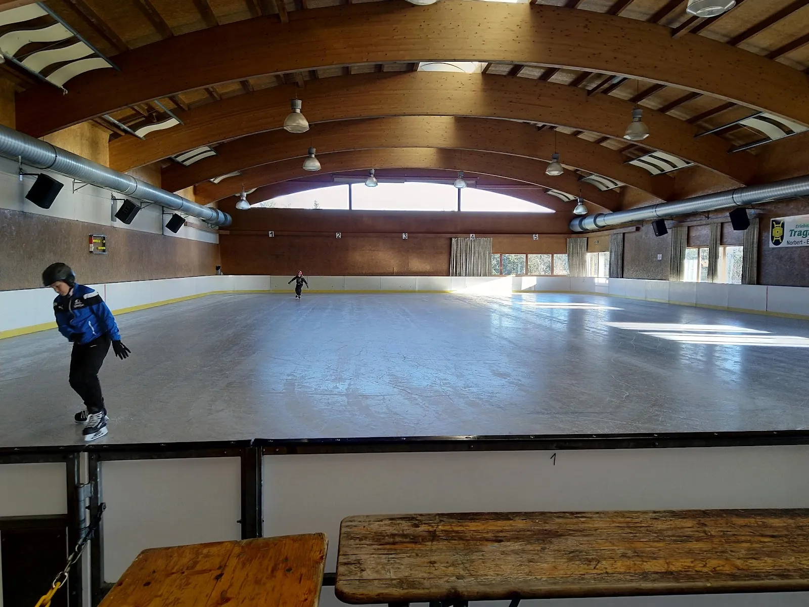 The ice of the Norbert-Eder-Halle in Tragwein under its curved timber roof, with a skater at the boards. — Eishalle Tragwein (Norbert-Eder-Halle)