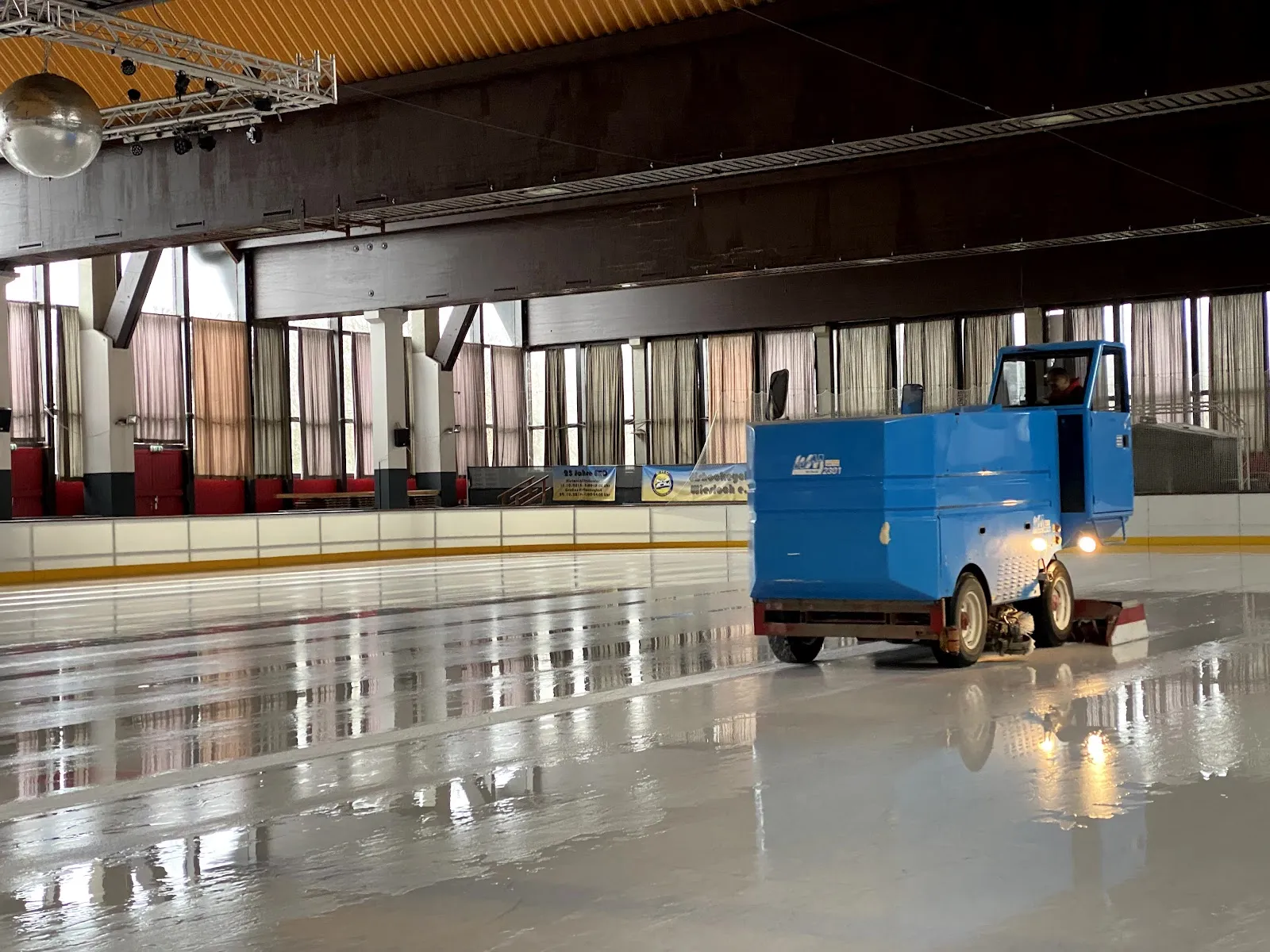 The resurfacer on fresh ice in the Eishalle Wiesloch, with the red stand seating and curtained windows behind the boards — Eishalle Wiesloch