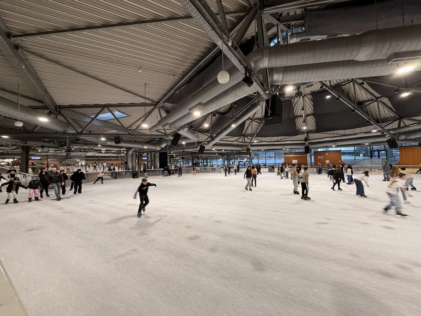 Ein öffentlicher Eislauf auf der weiten Eisfläche unter dem Stahlfachwerkdach, Läuferinnen und Läufer verteilen sich über die Bahn. – Eishalle Wischlingen