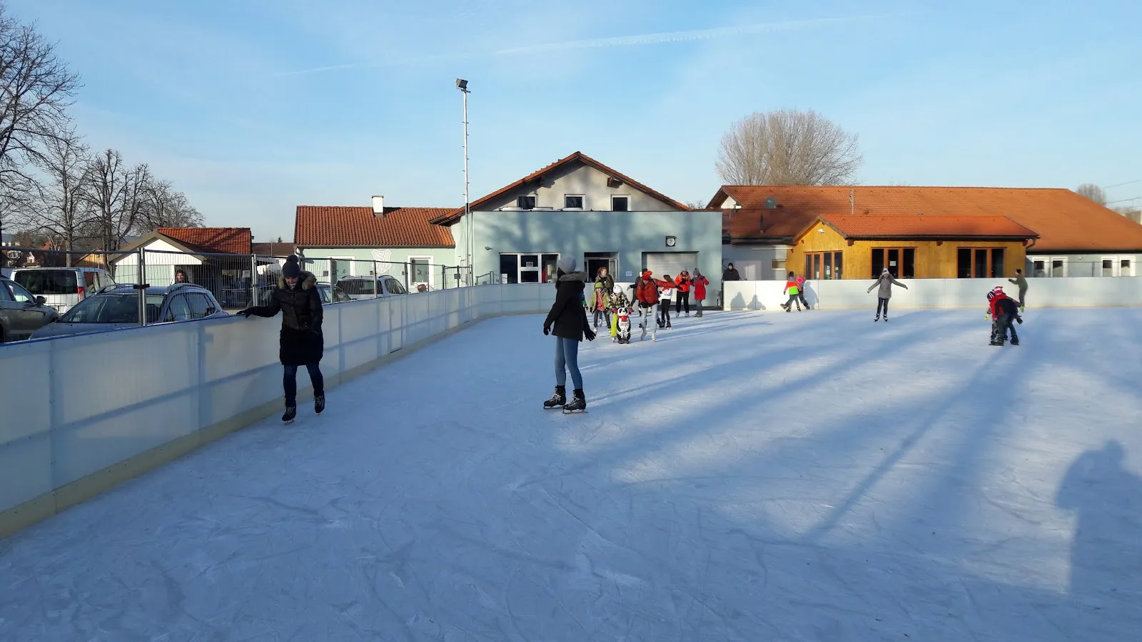 The Herzogenburg open-air ice rink with the clubhouse and sports-ground buildings behind the boards — Eislaufplatz Herzogenburg