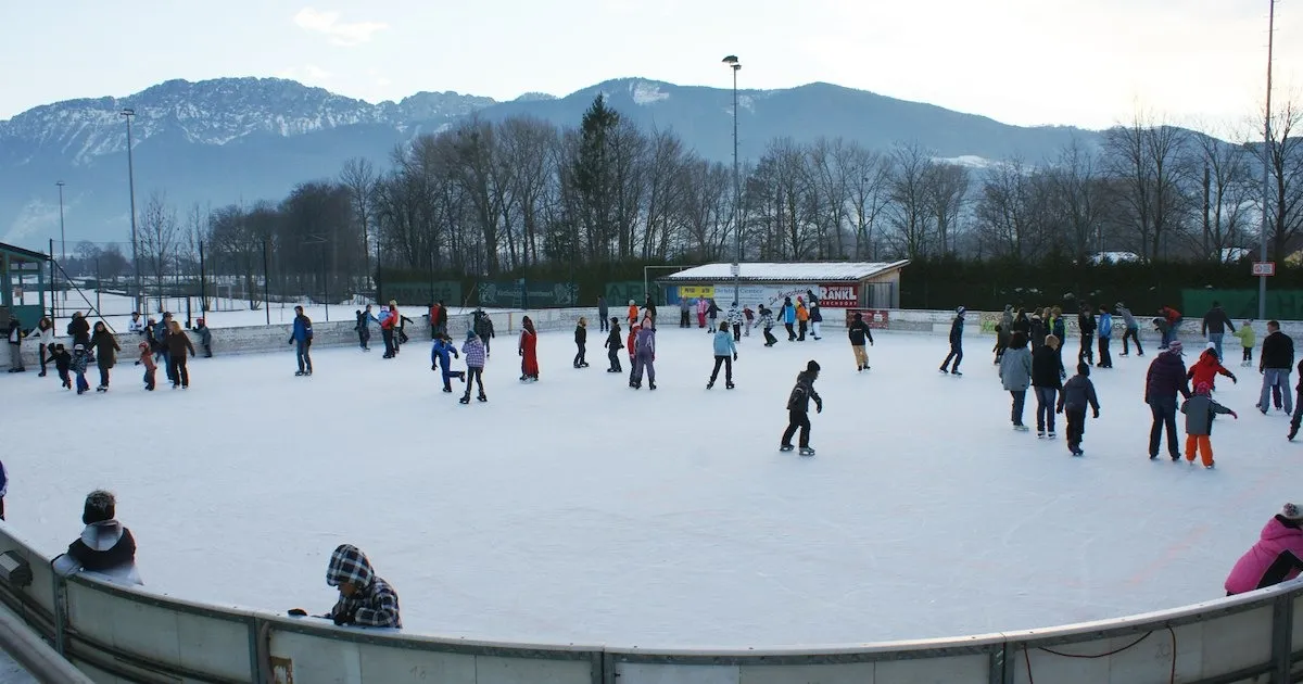 Skaters crowding the outdoor ice rink in Kirchdorf an der Krems on a winter afternoon with the mountains behind – Eislaufplatz Kirchdorf