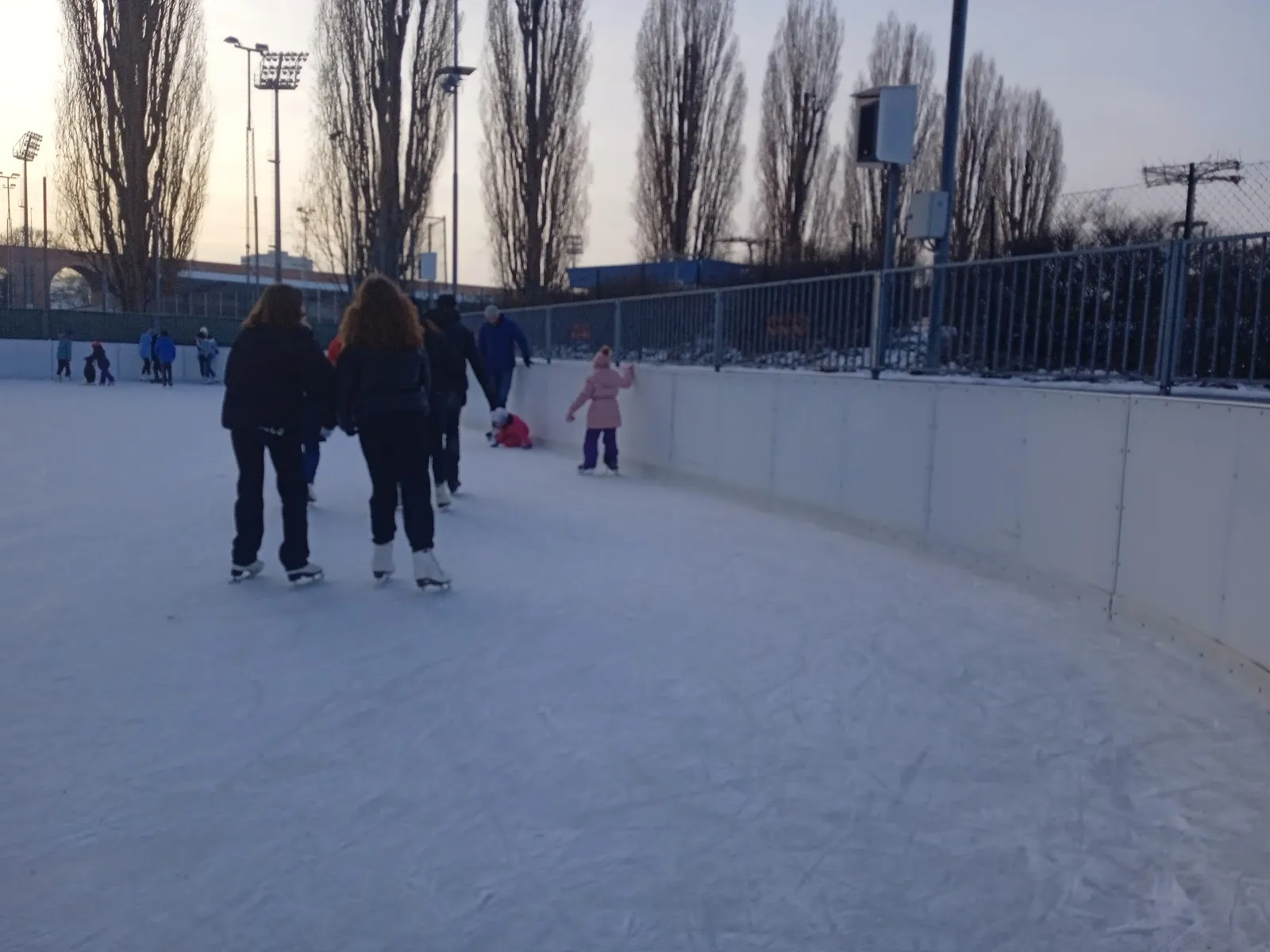 Die Freiluft-Eisbahn in Mattersburg mit Eisläufern auf der Fläche und den Banden an der Seite. – Eislaufplatz Mattersburg