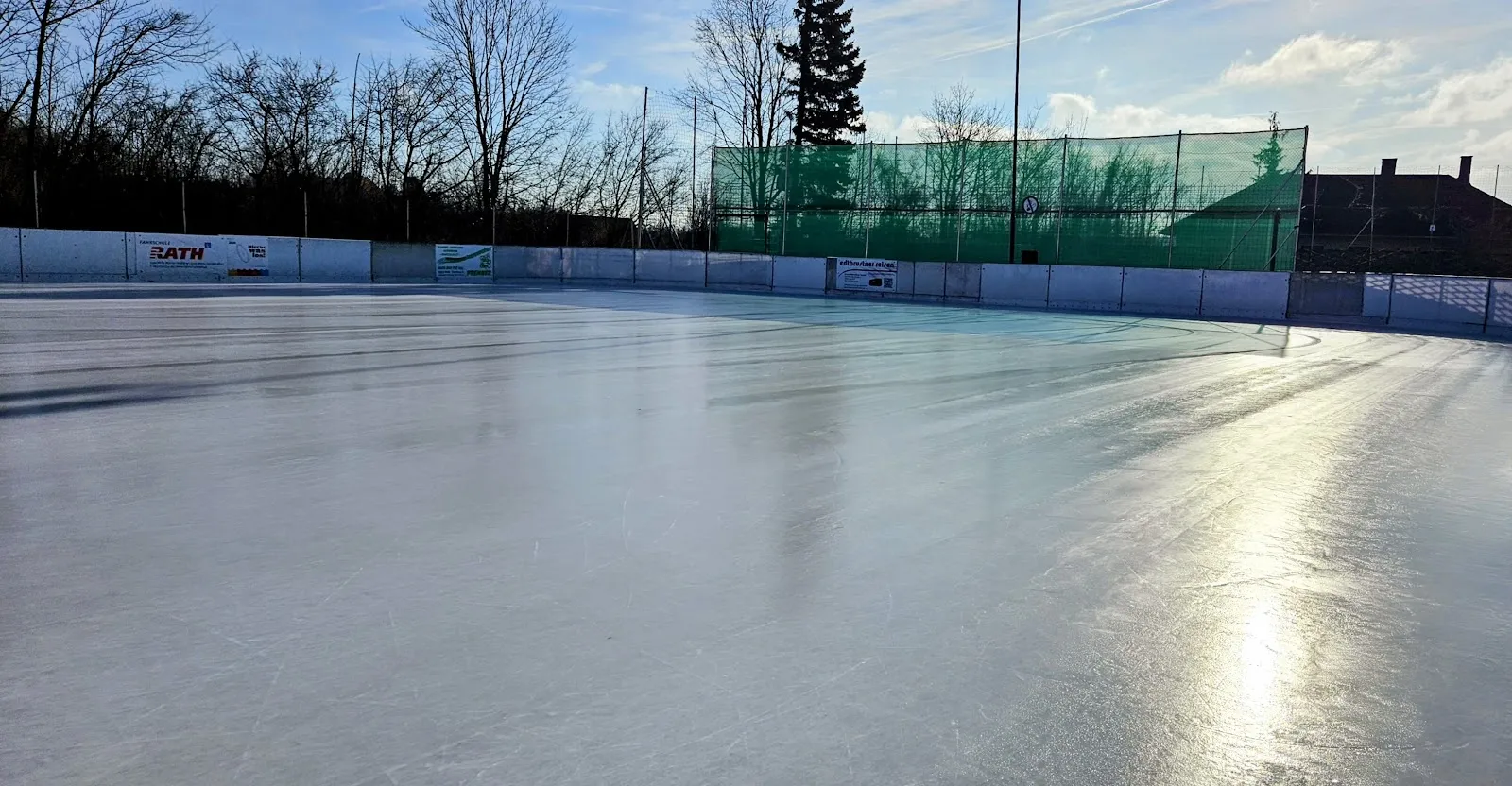 The smooth grey ice of the Melk open-air rink with the fence and bare trees along the far edge. — Eislaufplatz Melk
