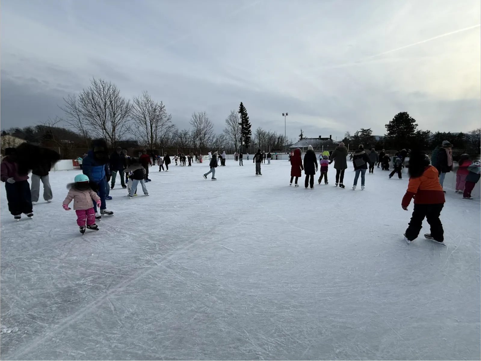 Skaters spread far across the wide Melk open-air rink under a cloudy winter sky. — Eislaufplatz Melk