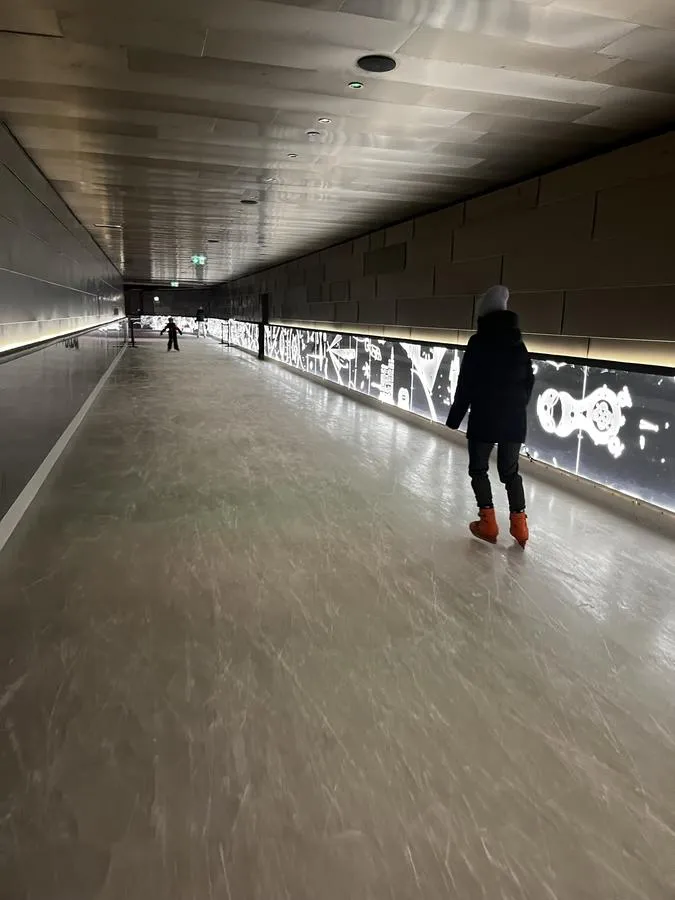 A skater on the covered stretch of the ice track, with the LED art panels glowing along the wall. – Eislaufplatz Silvretta Therme Ischgl