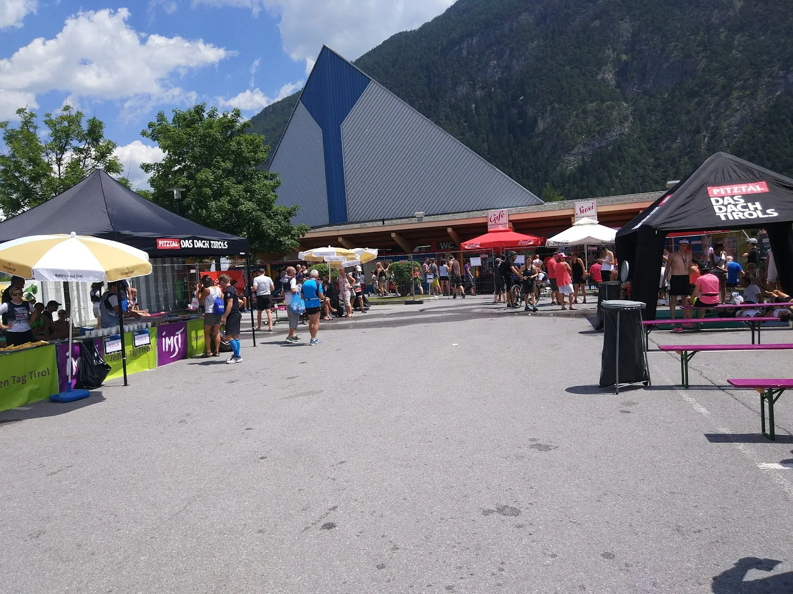 The Imst Sportzentrum forecourt with market-style stalls, benches and mountains rising behind. — Eislaufplatz Sportzentrum Imst