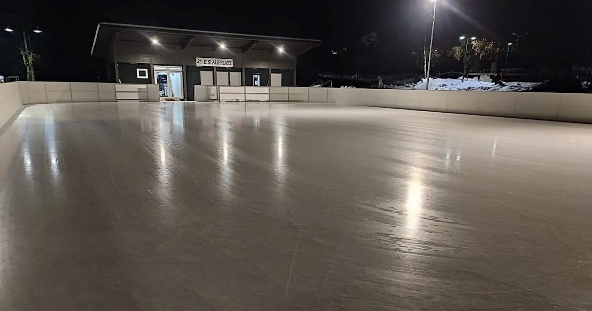 The floodlit Wagrain artificial ice rink at night, an empty ice surface in front of the rink building — Kunsteisbahn Wagrain