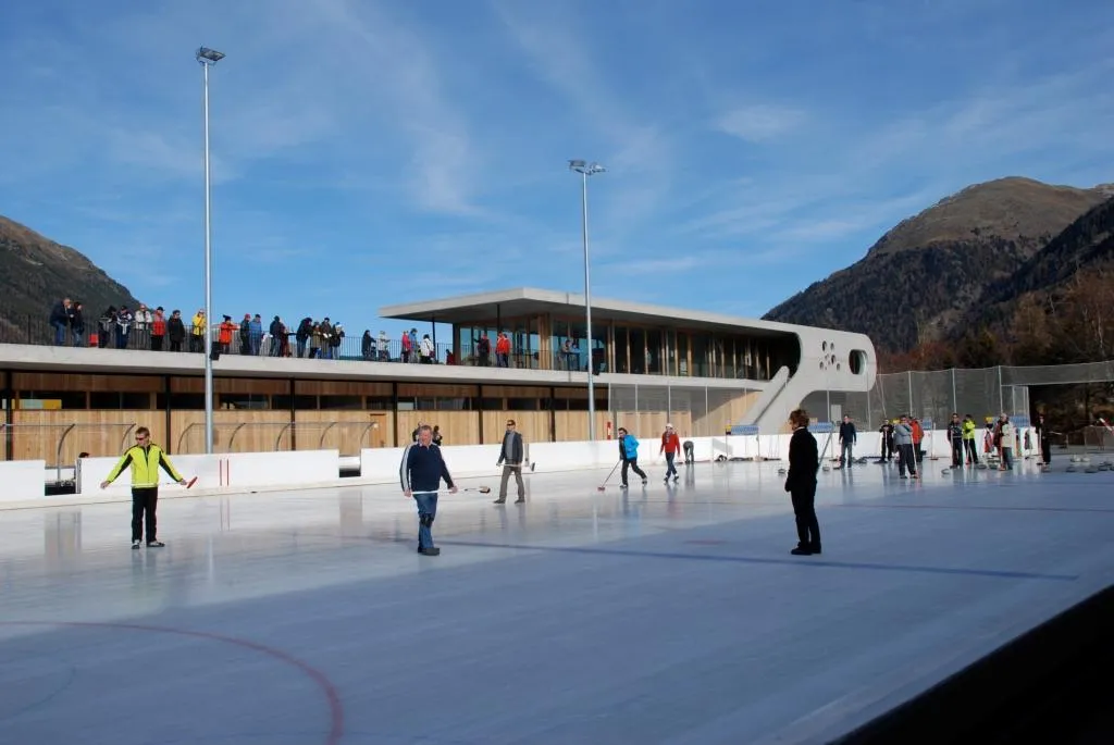 Skaters at a distance on the open-air rink of the Promulins Arena, Samedan, with the mountains behind – Eisplatz Promulins Arena