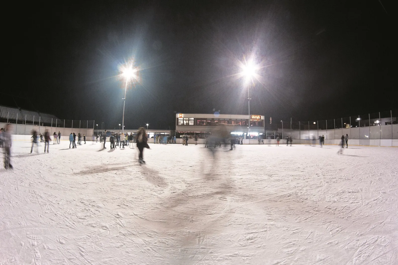 The open-air ice rink of the Eissportanlage at the Donaubad in Neu-Ulm in the evening, with floodlit ice and skaters in the distance. — Eissportanlage Donaubad
