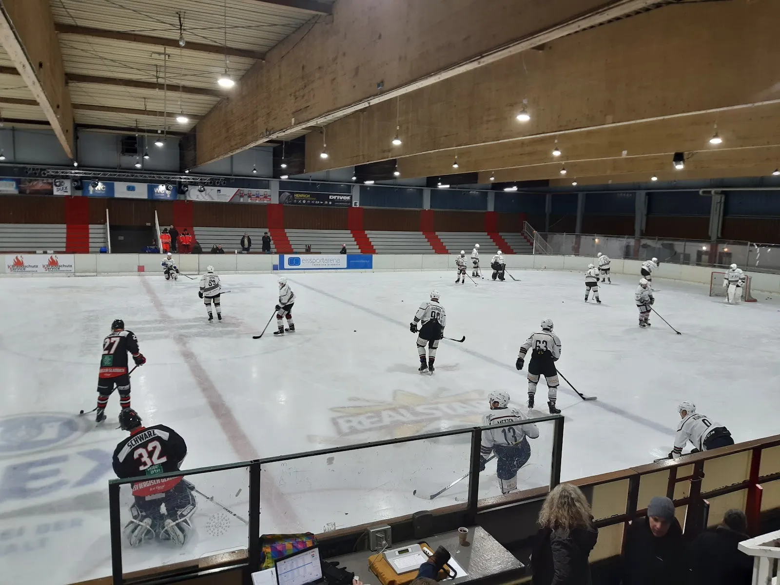 An ice hockey game in play at the Bergisch Gladbach ice arena, players across the rink under the wooden roof with the stands behind the boards. — Eissportarena Bergisch Gladbach