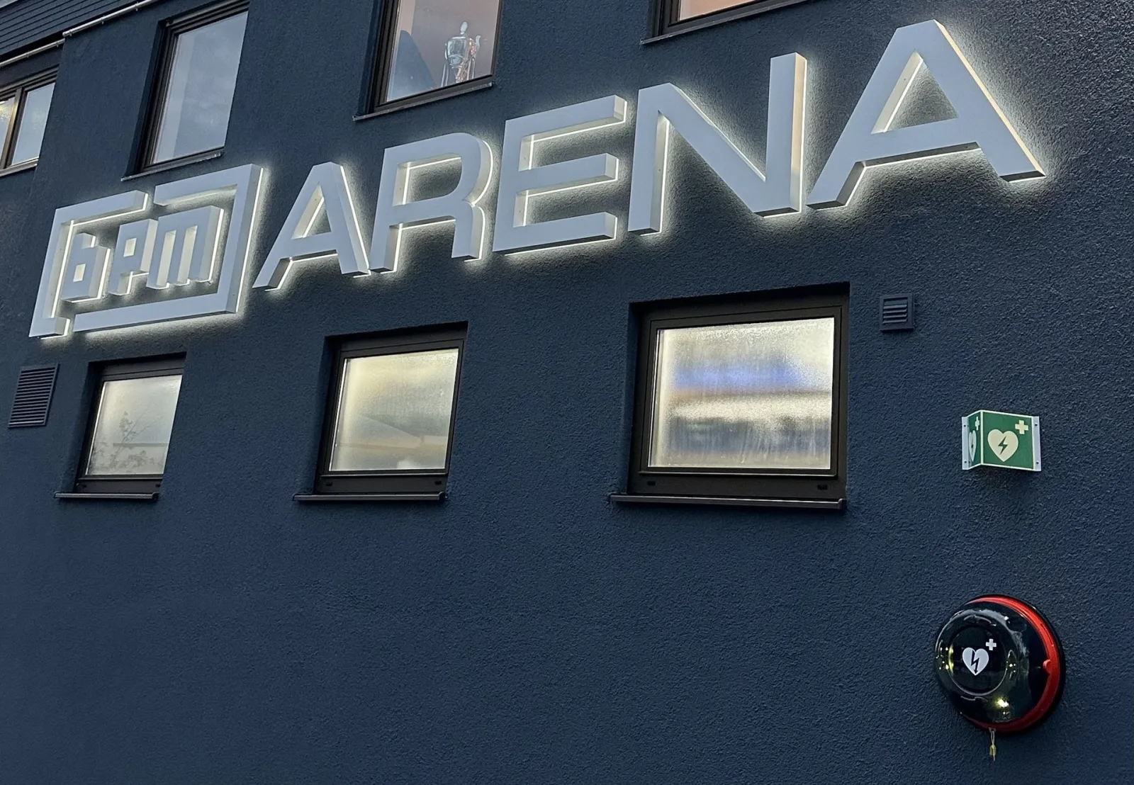 The BPM ARENA lettering lit on the dark upper façade of the Lindau ice arena building, with its windows, seen from outside. — Eissportarena Lindau (BPM-Arena)