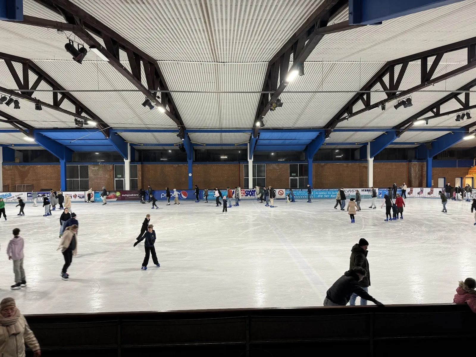 A public skating session at the Osnabrück ice centre, skaters spread across the ice under the blue-and-white steel roof structure. — Eissportcenter Osnabrück