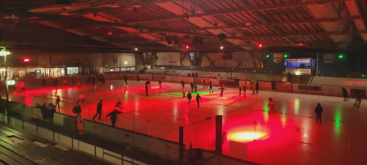 Läufer beim Publikumslauf auf dem rot beleuchteten Eis bei einer Eisdisco in der Arena Bad Wörishofen, mit den Glasbanden und dem Holzdach darüber. – Eissporthalle Bad Wörishofen (yourlife Immobilien Arena)