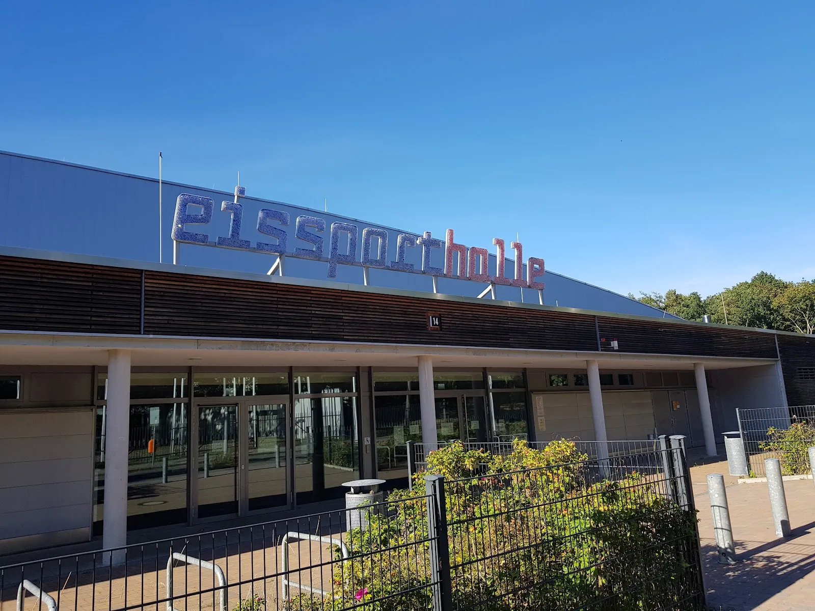 The hall's metal-clad front with its large eissporthalle lettering over a glazed colonnaded entrance, under a clear blue sky. — Eissporthalle Charlottenburg (PO9)