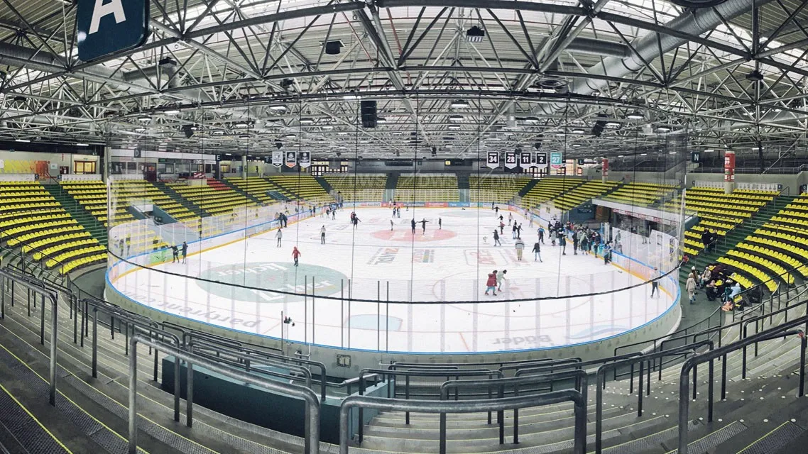 Die Eishalle der Eissporthalle Frankfurt von den Rängen aus gesehen, unter ihrem Stahldach, mit einem Publikumslauf weit unten auf dem Eis – Eissporthalle Frankfurt