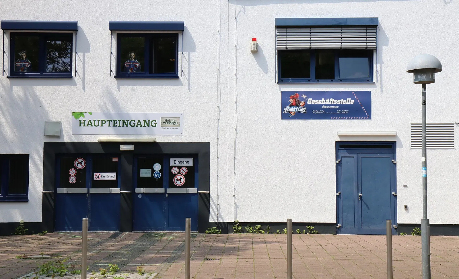 Der „Haupteingang“ der Eissporthalle Iserlohn an einer weißen Fassade mit blauen Türen. – Eissporthalle Iserlohn