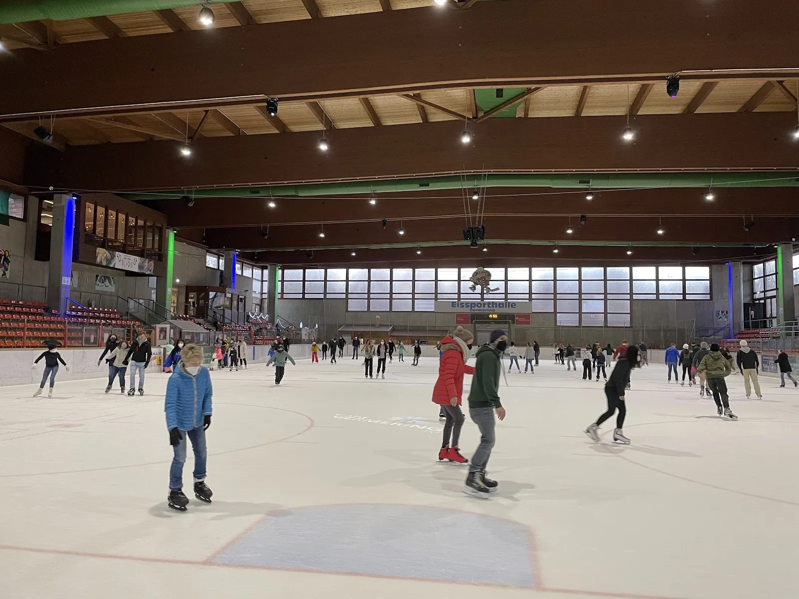 Skaters on the ice of the Polariom ice hall in Germering during a public session, with the dark timber roof and the clerestory windows along the far wall. — Eissporthalle Polariom Germering
