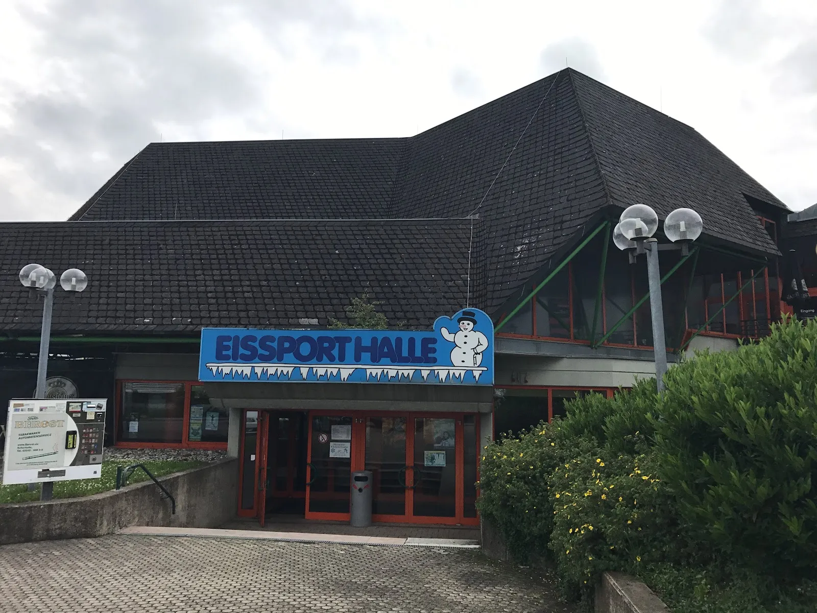 The dark-roofed Eissporthalle Willingen with its blue snowman name sign above the red-framed entrance — Eissporthalle Willingen