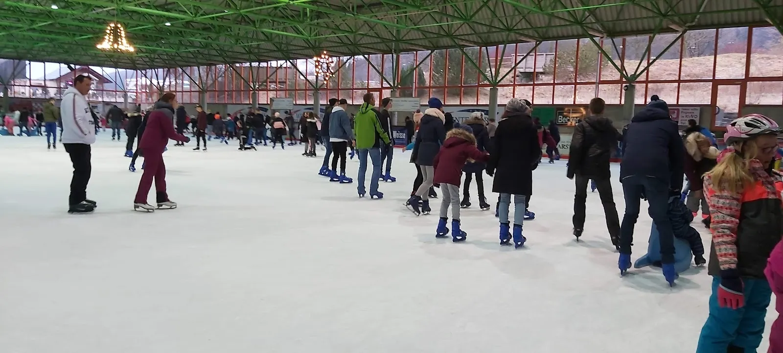 A busy public skating session on the ice of the Willingen ice hall, with skaters and families across the sheet under the green roof. — Eissporthalle Willingen