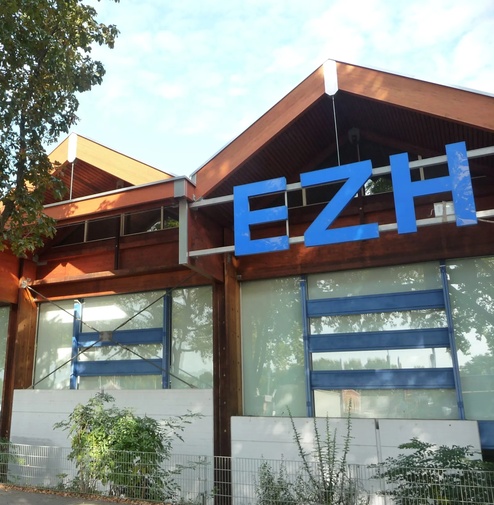 Das Gebäude des Eissportzentrums Herzogenried mit dem blauen EZH-Schriftzug am Dachrand – Eissportzentrum Herzogenried