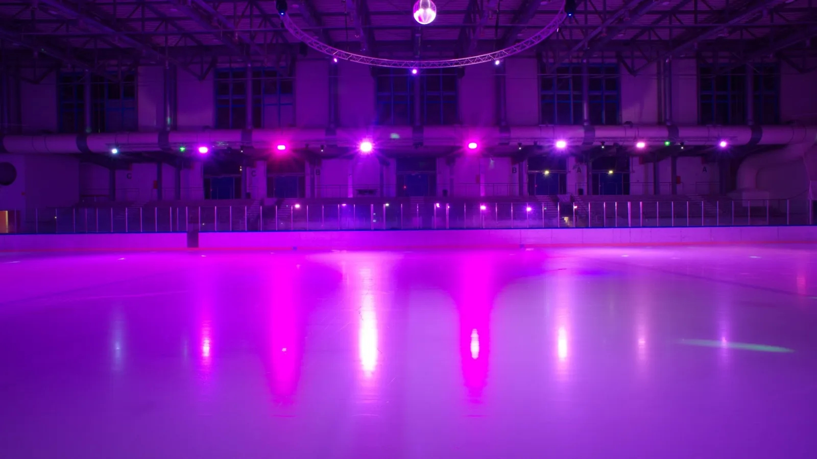 Das leere Eis in Pforzheim in rosa und violettem Scheinwerferlicht, dahinter Banden und Tribüne. – Eissportzentrum Pforzheim