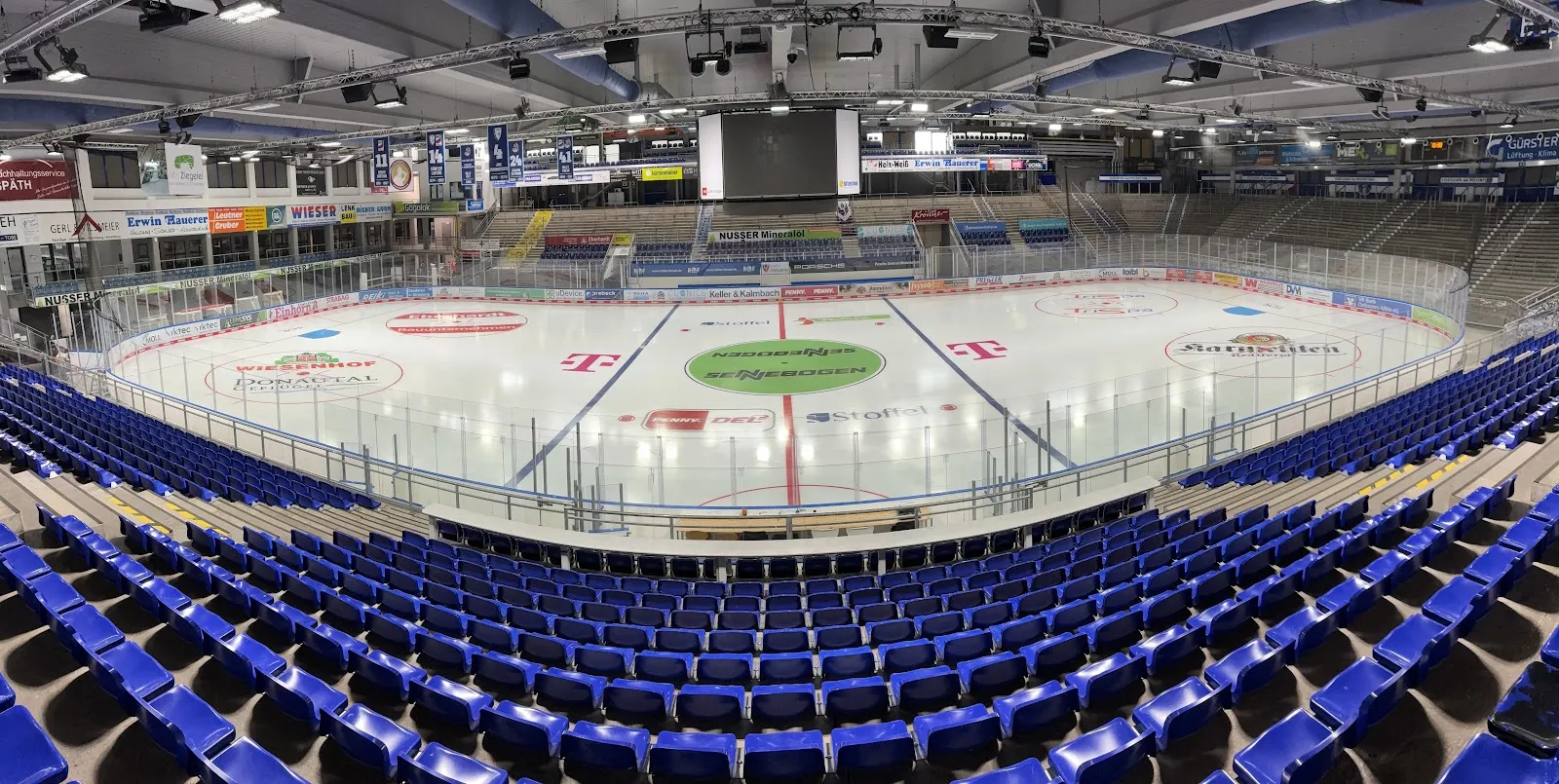 The stadium's single ice surface seen from the stands, with the blue seats curving around the rink and the centre-ice logo. — Eisstadion am Pulverturm