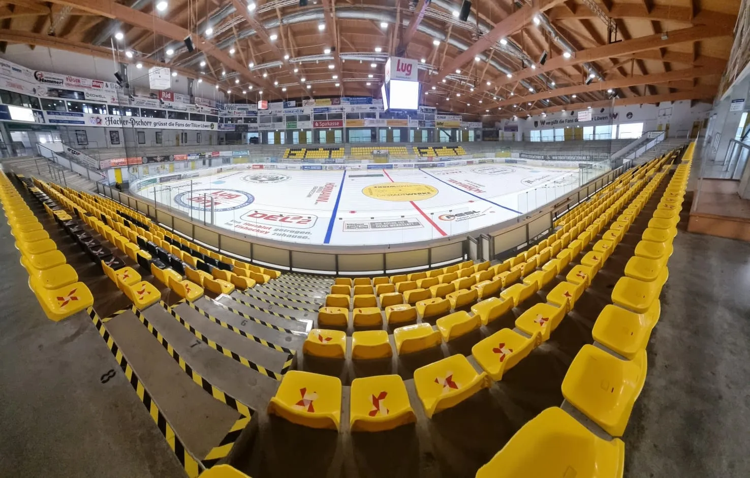 The empty ice of the Hacker-Pschorr Arena in Bad Tölz from the yellow stands, with the timber roof, the long side stands and the centre-ice markings. — Eisstadion Bad Tölz