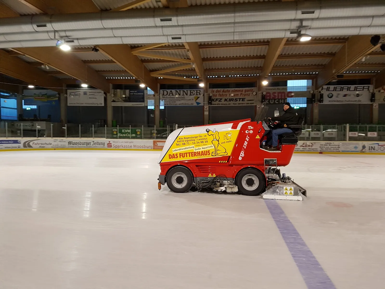 Die Eismaschine auf dem Eis der Clariant Arena in Moosburg, dahinter das Holzdach und die Sponsorenbanden – Eisstadion Clariant Arena