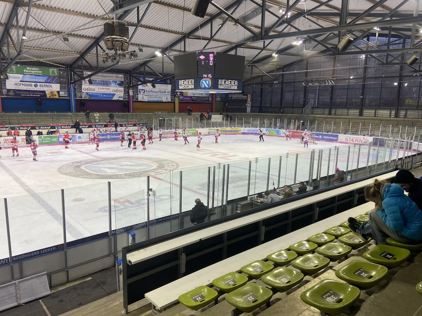 The arena from the stands: the ice surface under the steel roof with the boards and the far-end hockey play seen from a distance. — Eisstadion Deggendorf