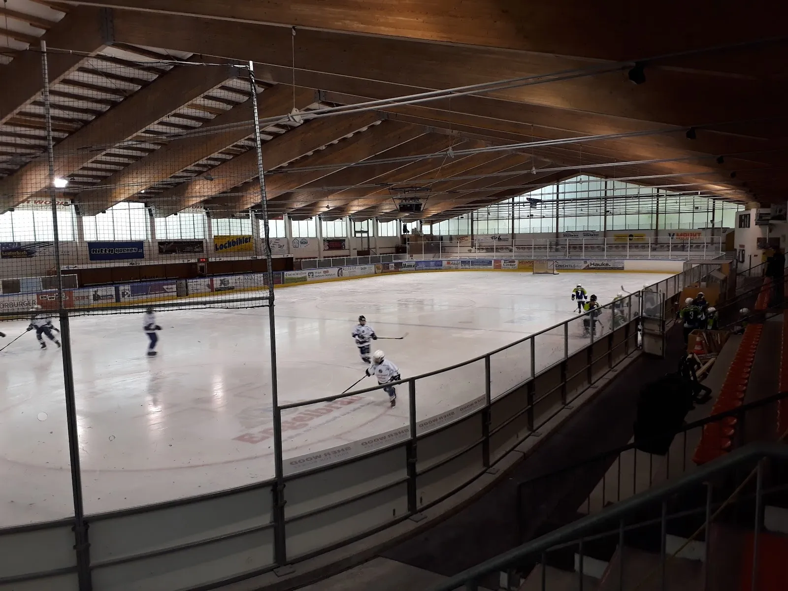 Ein Spieler auf dem Eis des Eisstadions Pfronten, von der Tribünenseite aus gesehen, unter dem Holzdach. – Eisstadion Pfronten