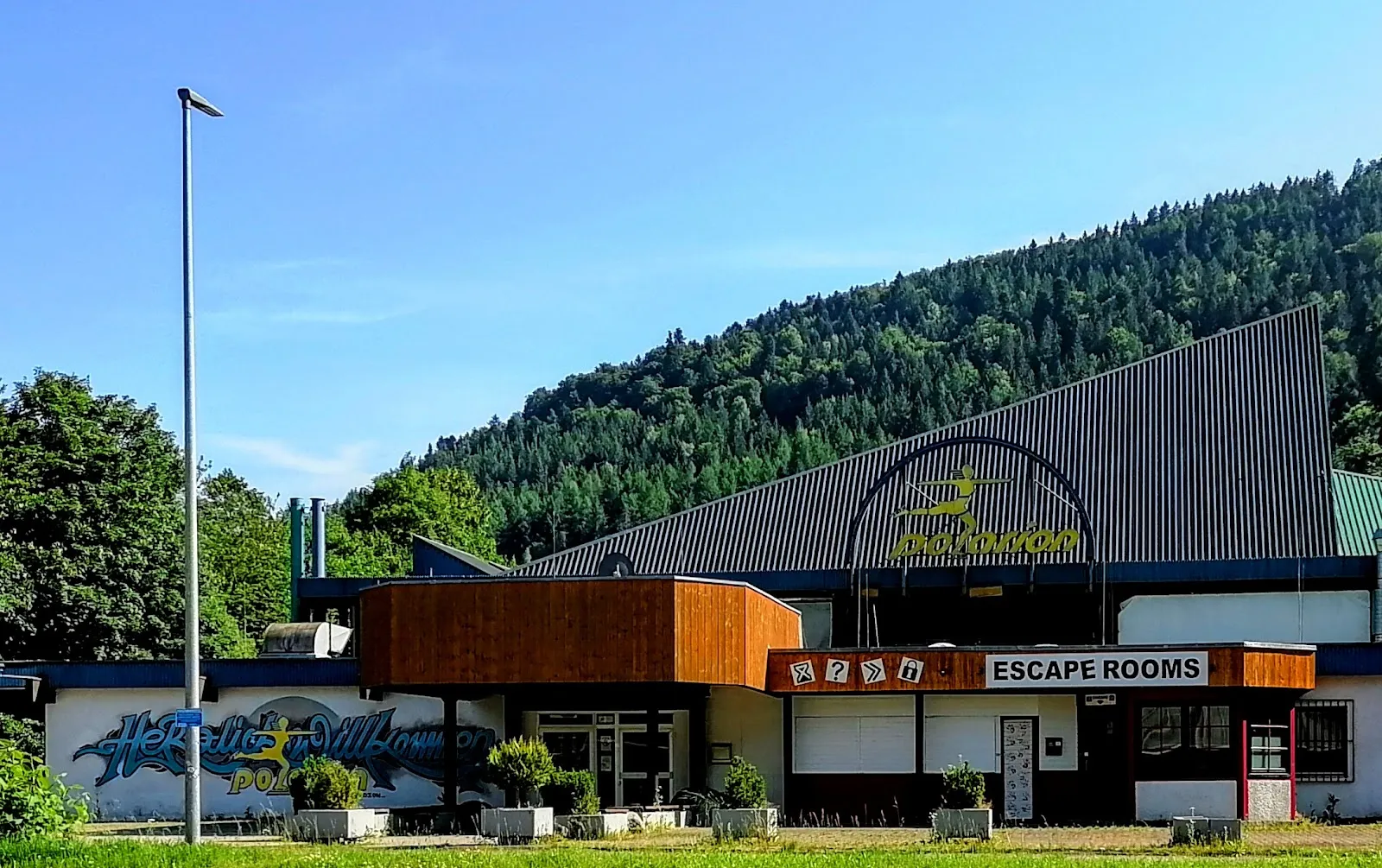 The Polarion ice stadium building in Bad Liebenzell with its dark roof and timber-clad entrance block, seen from the grass with the forested hillside behind — Eisstadion Polarion