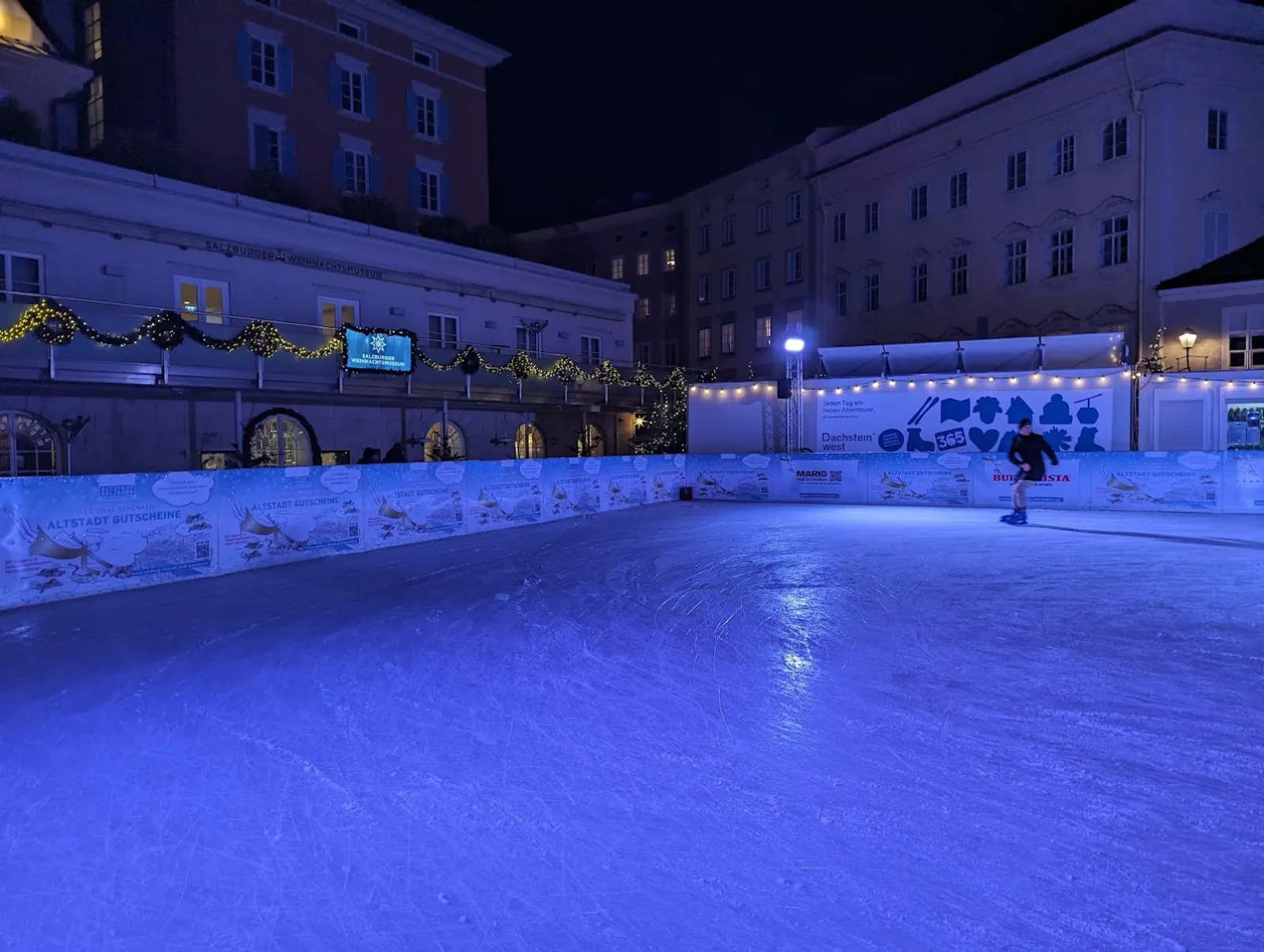 The blue-lit ice of the Eiszauber on the Mozartplatz in Salzburg at night, with the boards and the historic buildings around the square. — Eiszauber am Mozartplatz