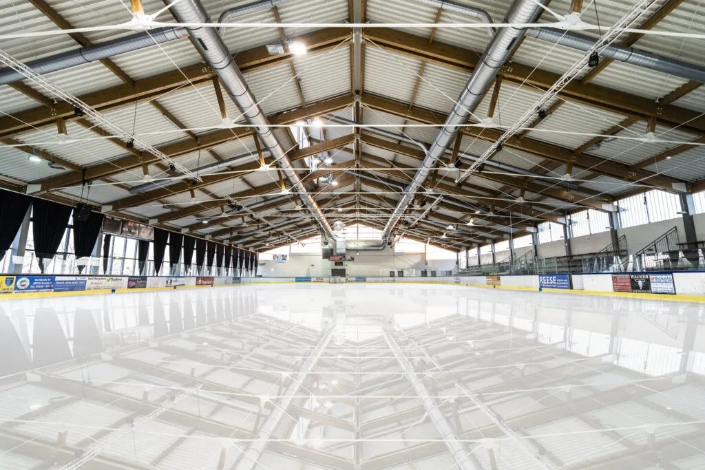 The empty ice of the Elbe Ice Stadion under its timber roof trusses, with the boards along the far side — Elbe Ice Stadion