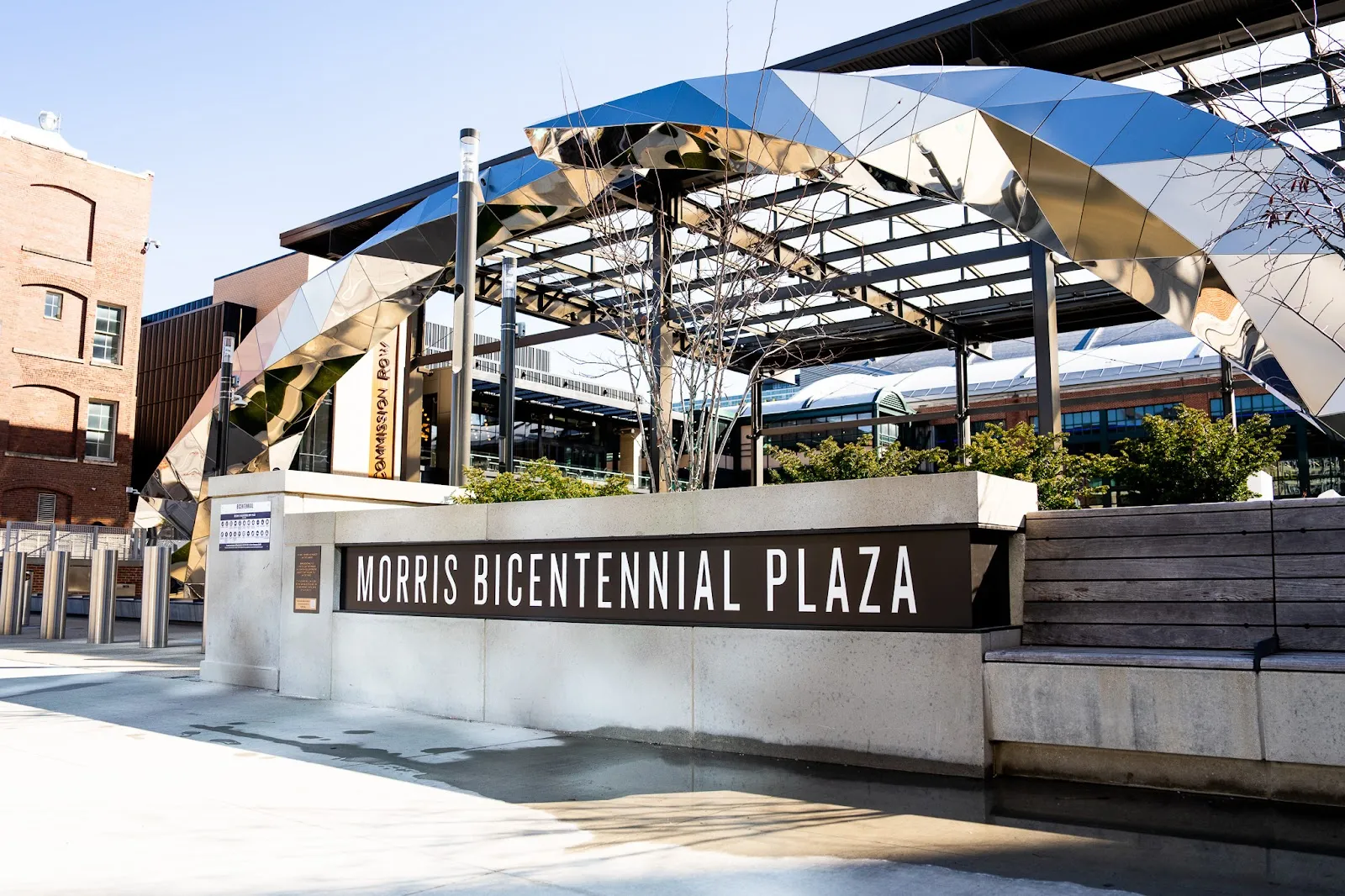 The Morris Bicentennial Plaza sign and the faceted steel pavilion roof over the plaza where the rink is set up each winter. — Elevance Health Rink at Morris Bicentennial Plaza