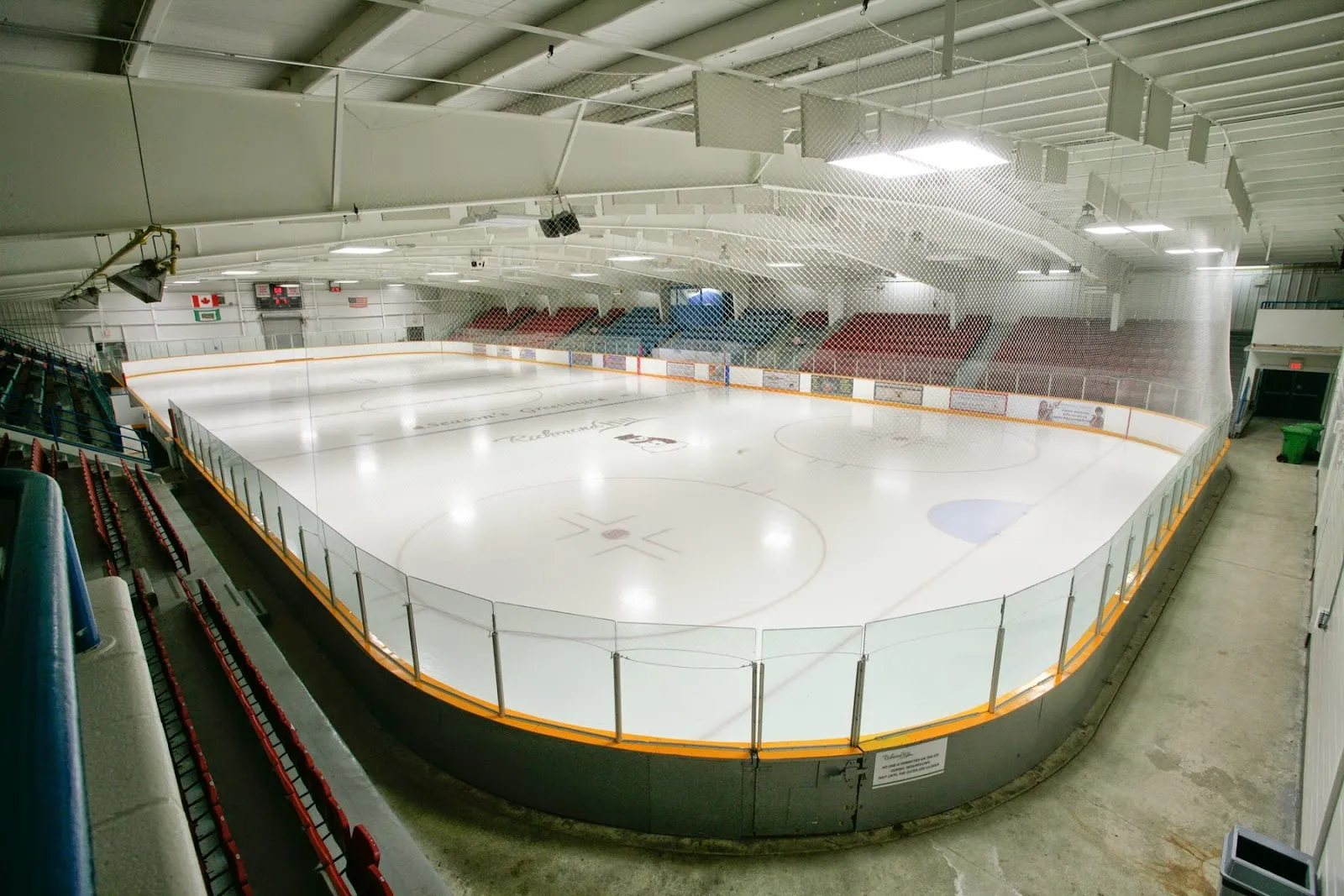 La pista completa desde los asientos: hielo limpio, vallas rojas y blancas y las gradas a lo largo de un costado. — Elgin Barrow Arena (Richmond Hill)