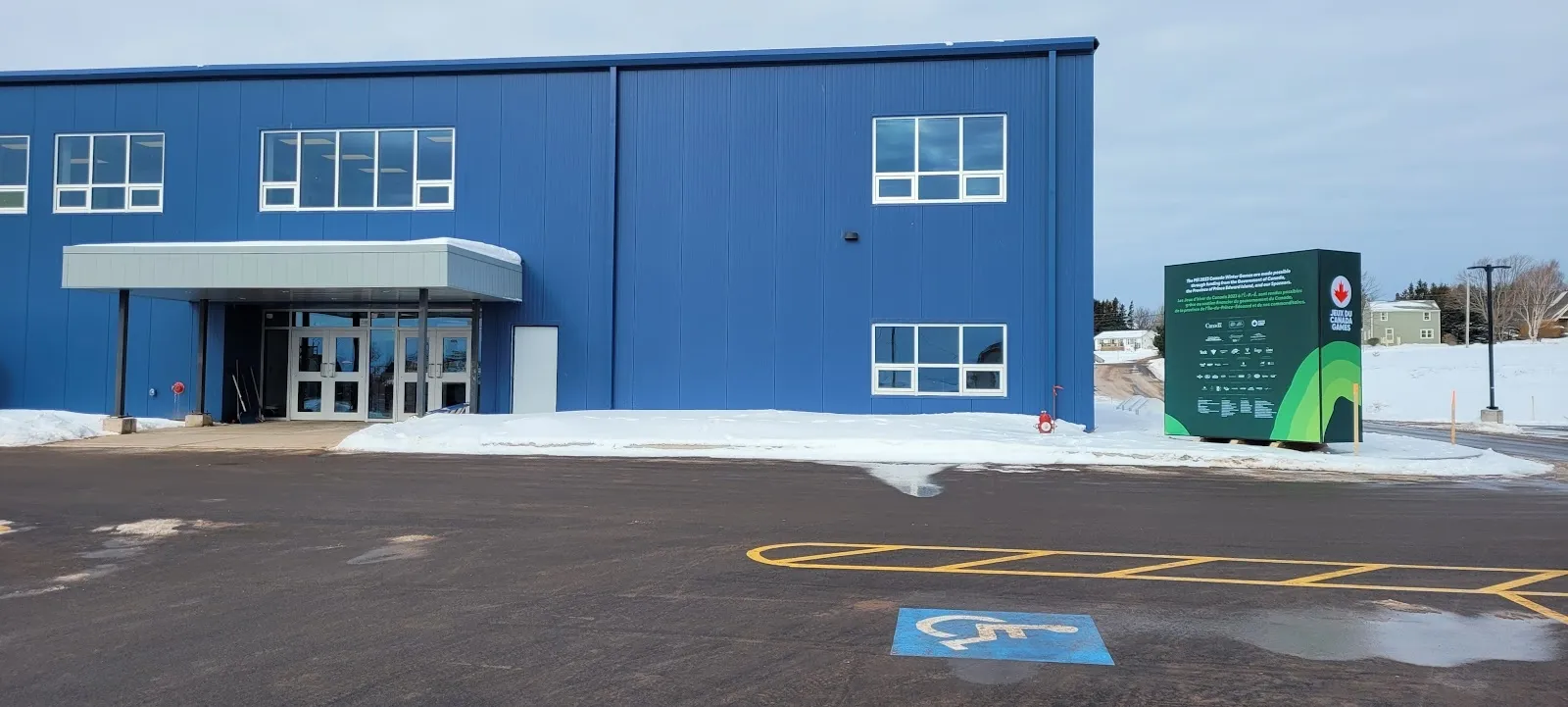 The blue-clad entrance block of the Eliyahu Wellness Centre with a glazed doorway and a small green sign, seen across the car park. — Eliyahu Wellness Centre