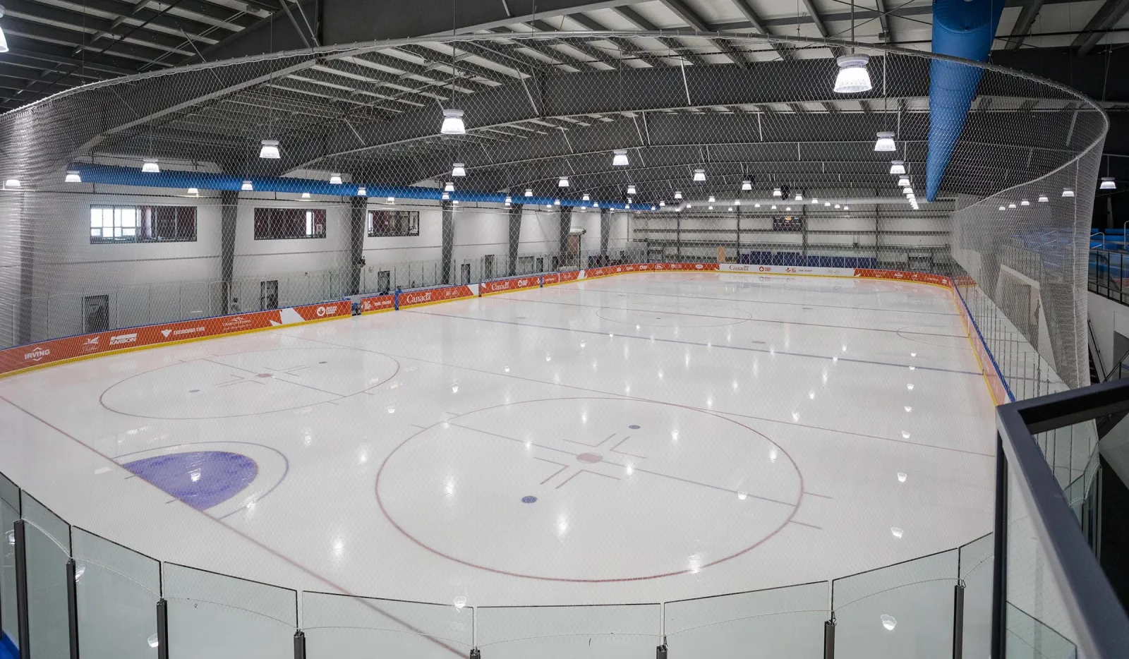The empty ice sheet inside the Eliyahu Wellness Centre arena, seen from the stand with the blue boards and steel roof above — Eliyahu Wellness Centre