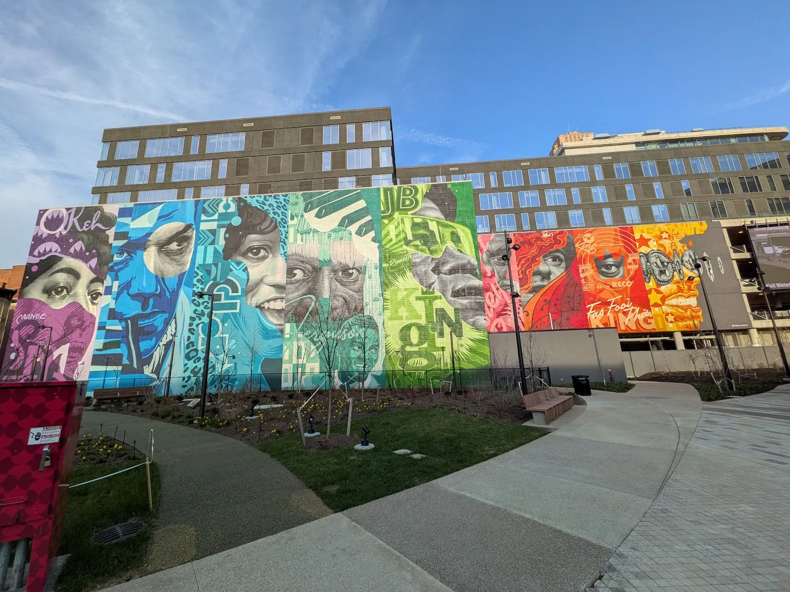 El muro con mural de Elm Street Plaza en el centro de Cincinnati, visto al otro lado del césped y los caminos de la plaza — UC Health Ice Rink at Elm Street Plaza