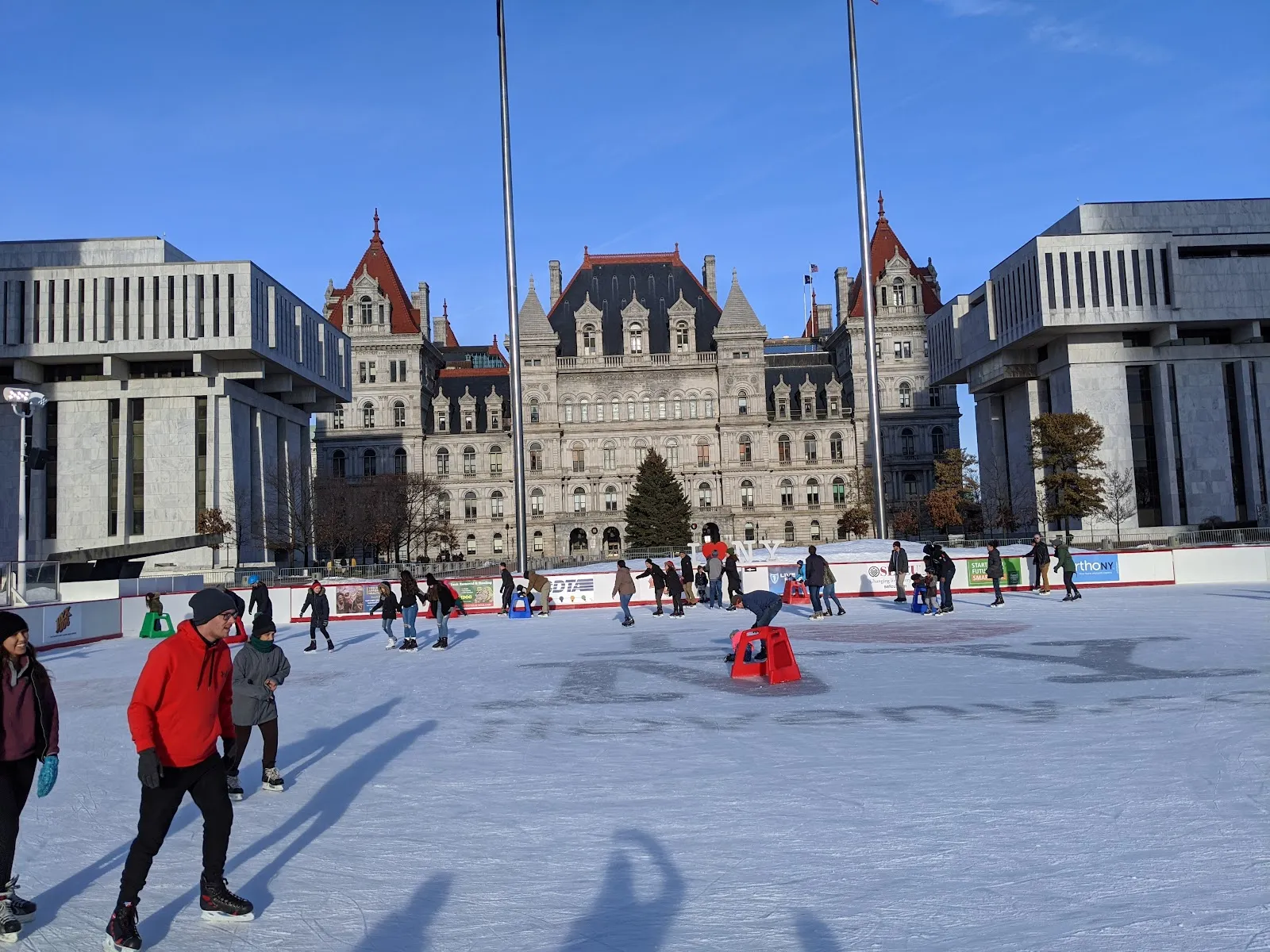 Skaters on the Empire State Plaza ice rink with the State Capitol and plaza buildings behind — Empire State Plaza Ice Rink