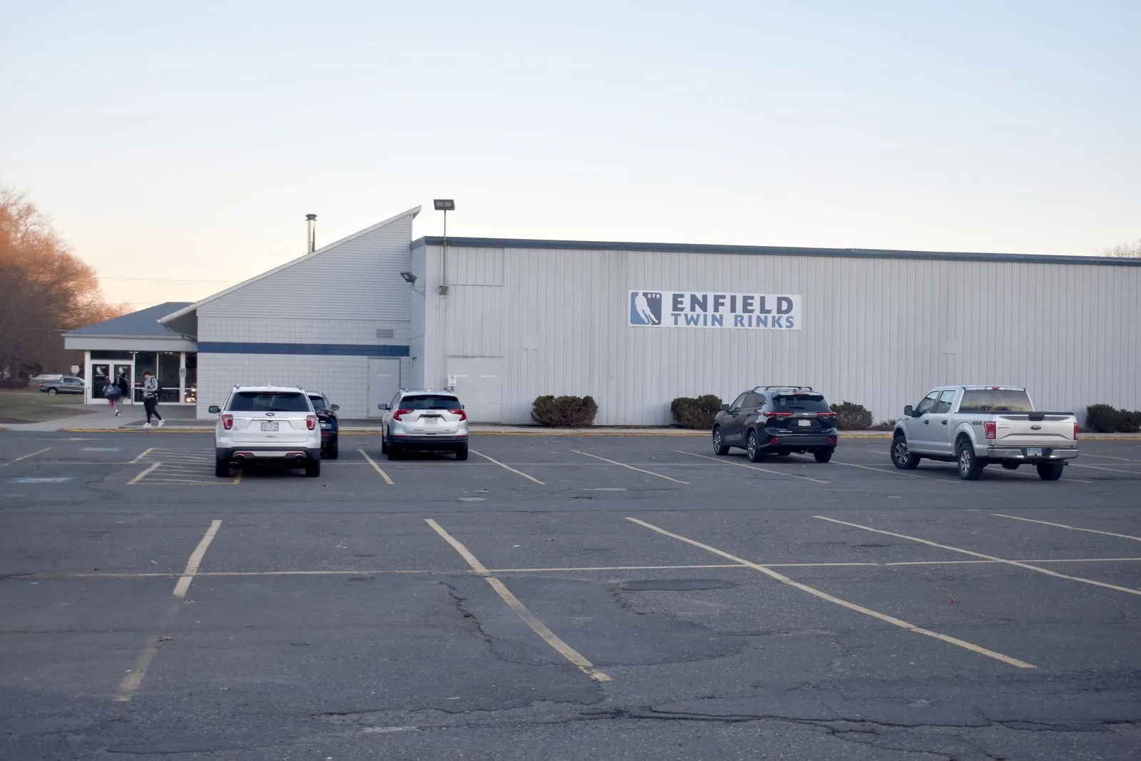 Front and side of the Enfield Twin Rinks building at dusk, with an 'ENFIELD TWIN RINKS' wall sign and parking lot in the foreground. — Enfield Twin Rinks
