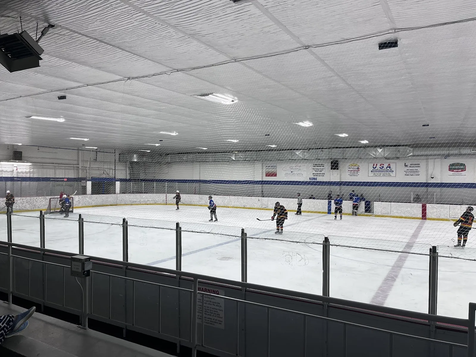 A public session on a wide sheet seen over the boards, skaters spread across the ice under a pale ceiling with a green bench along the far side. — Enfield Twin Rinks