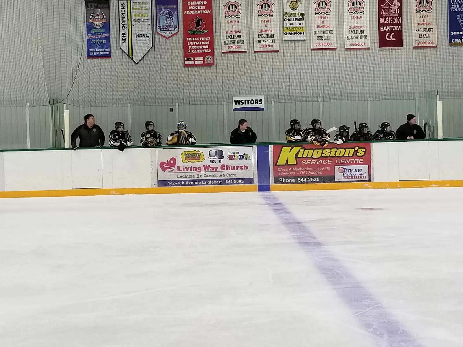 The ice at Englehart Arena with the blue line, sponsor boards and a row of team banners hanging on the far wall. — Englehart and Area Community Arena Complex
