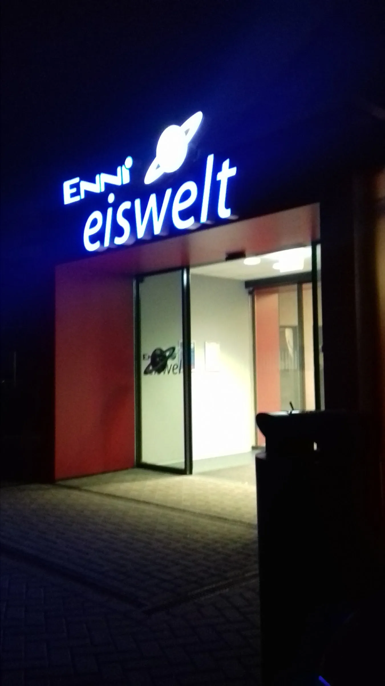 Der leuchtende Schriftzug enni eiswelt über dem rot gerahmten Eingang der Eishalle in Moers bei Nacht – enni.eiswelt