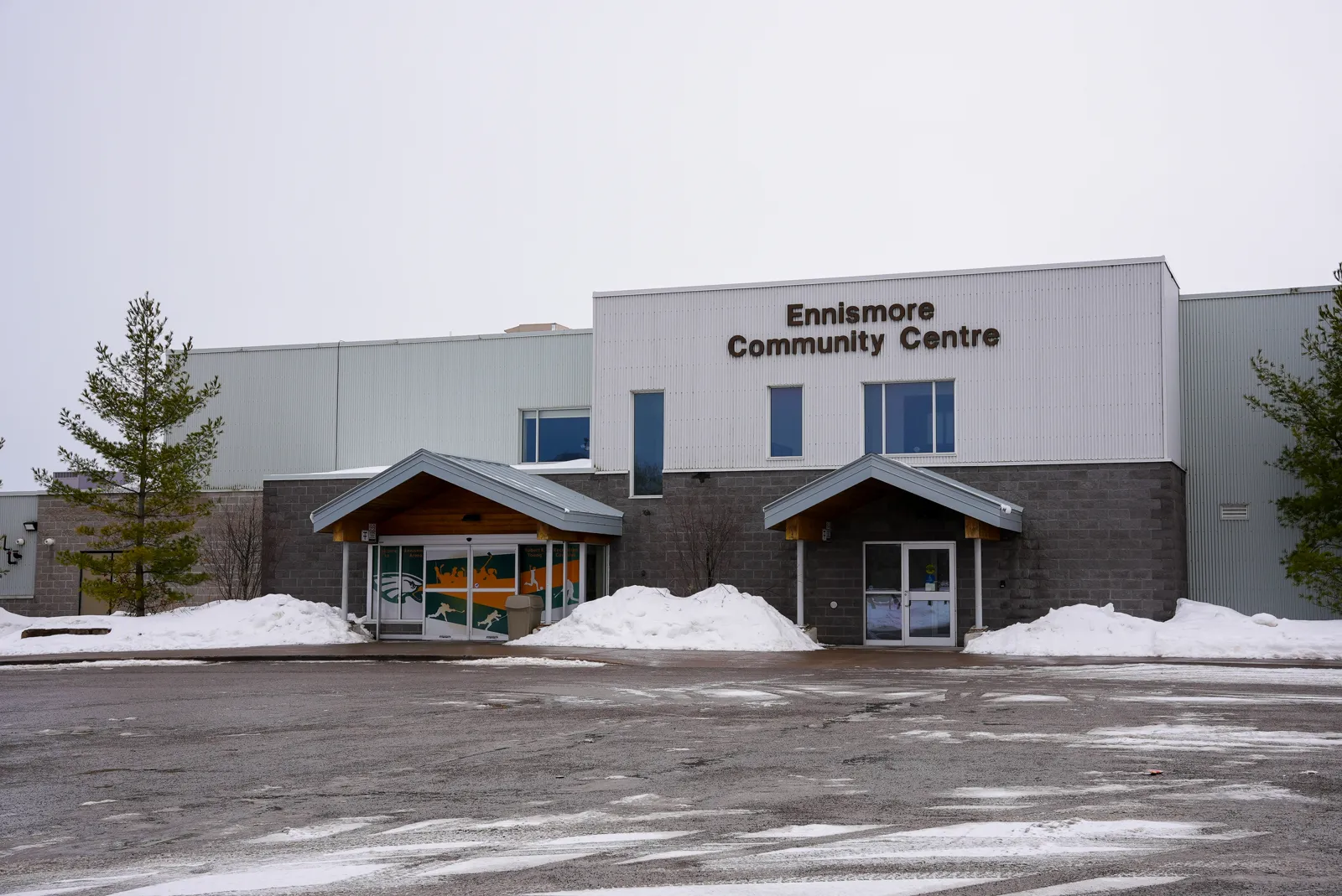 La entrada del Ennismore Community Centre en invierno, con dos pórticos de madera a dos aguas bajo el muro gris de la arena. — Ennismore Community Centre