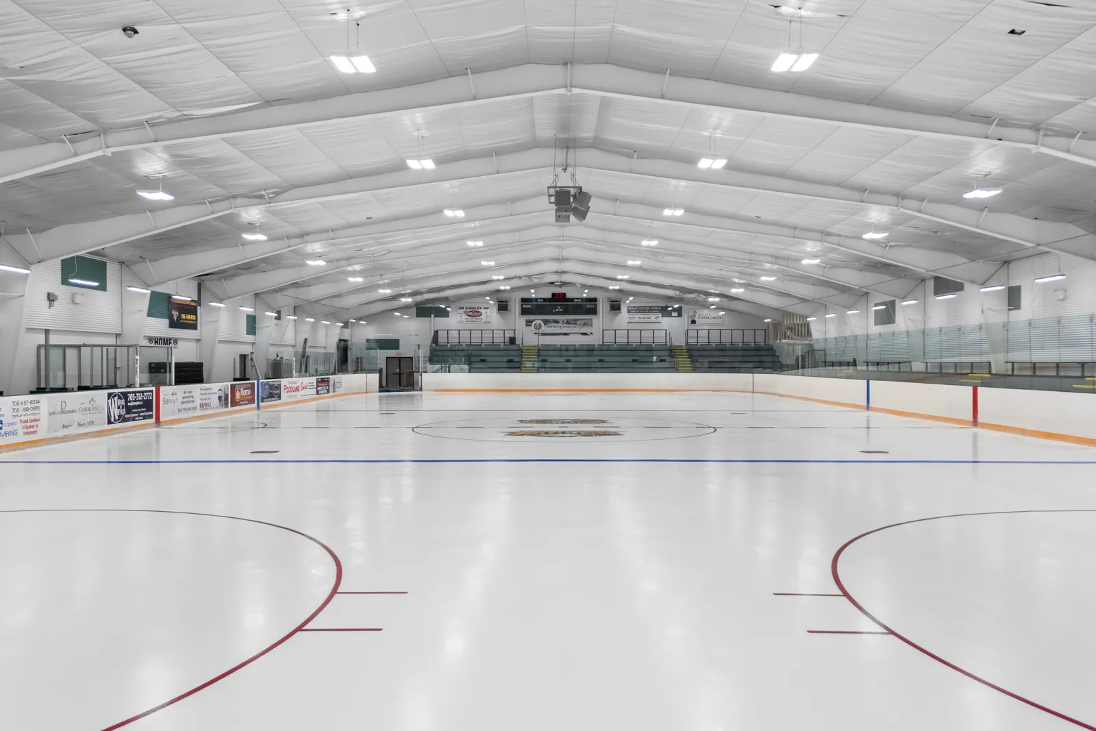 La pista renovada bajo una brillante iluminación blanca en el techo, con vallas de remates verdes y asientos a un lado. — Ennismore Community Centre