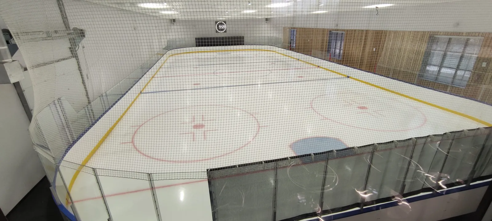 The empty ice sheet of the Eskimo arena in Tyumen seen from above the boards, with red and blue lines and glass panels — Eskimo Ice Arena Tyumen