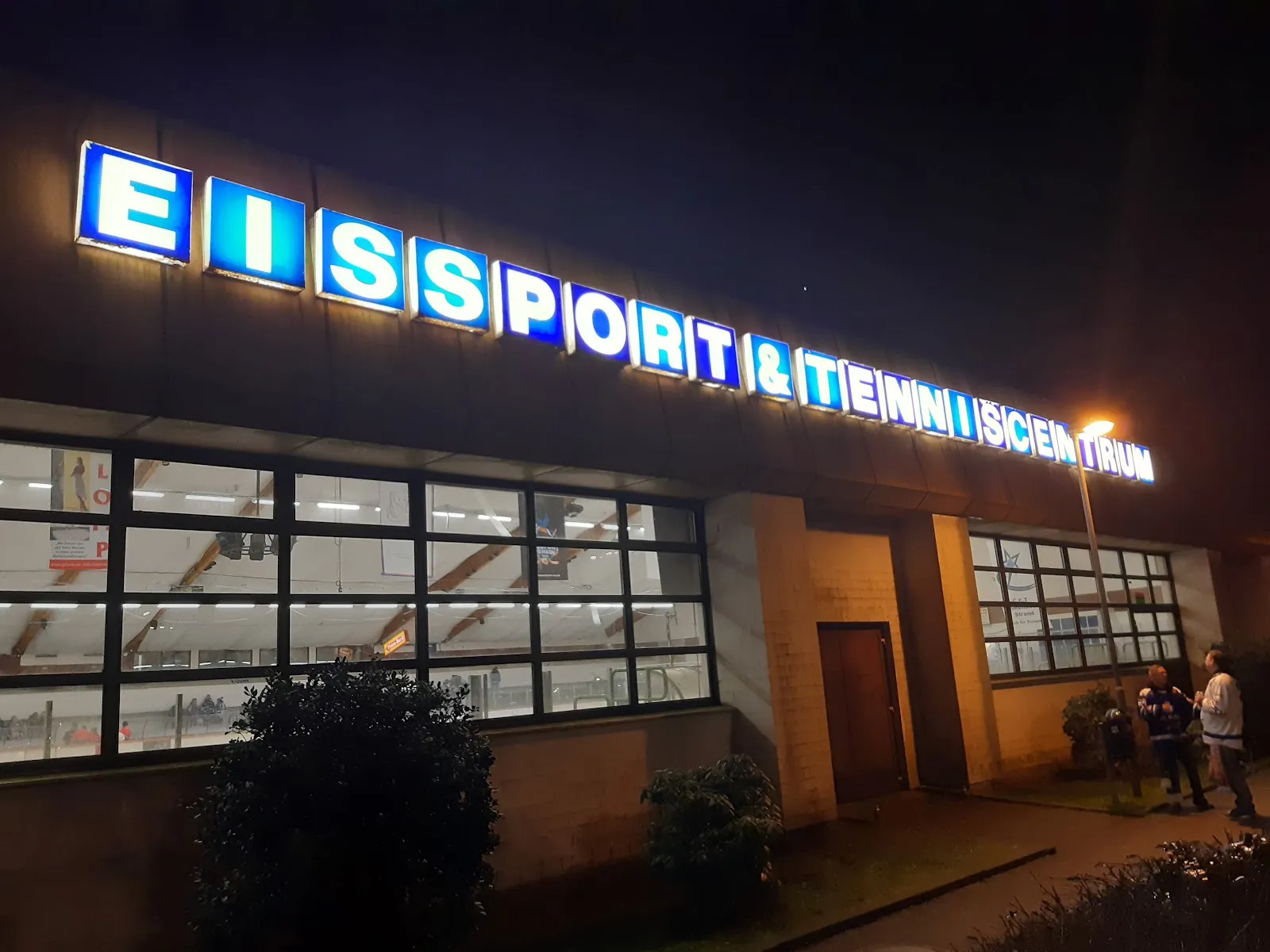 Der beleuchtete Schriftzug Eissport und Tenniscentrum über der verglasten Front der Halle in Timmendorfer Strand, bei Nacht gesehen – ETC Eishalle Timmendorfer Strand